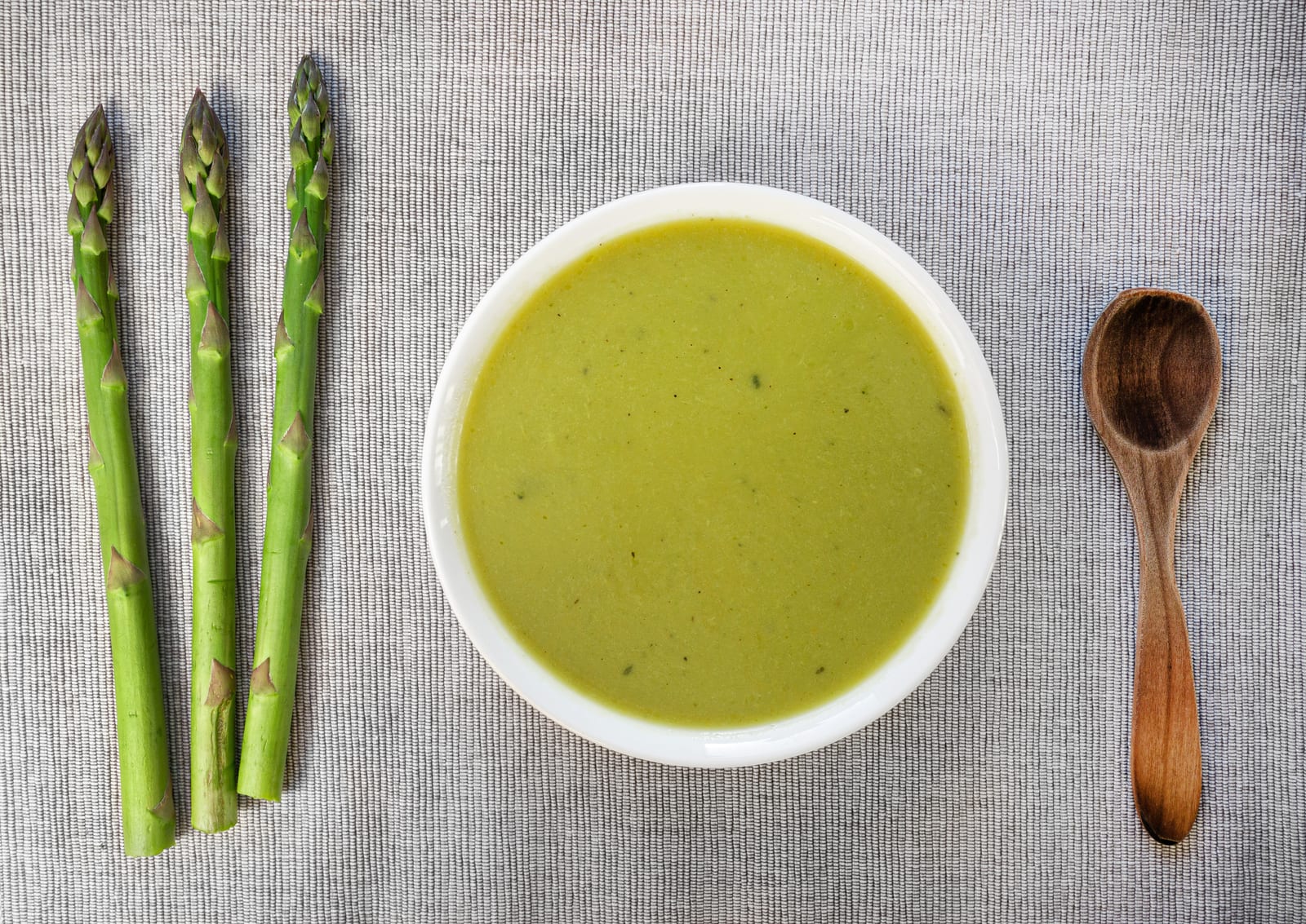 A bowl of asparagus soup with asparagus spears alongside