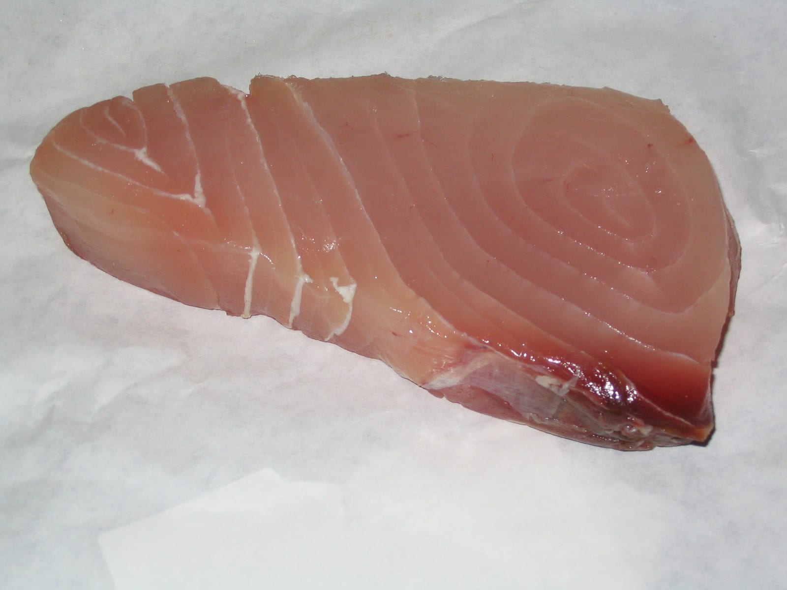 A thick cut of raw fish on a white surface