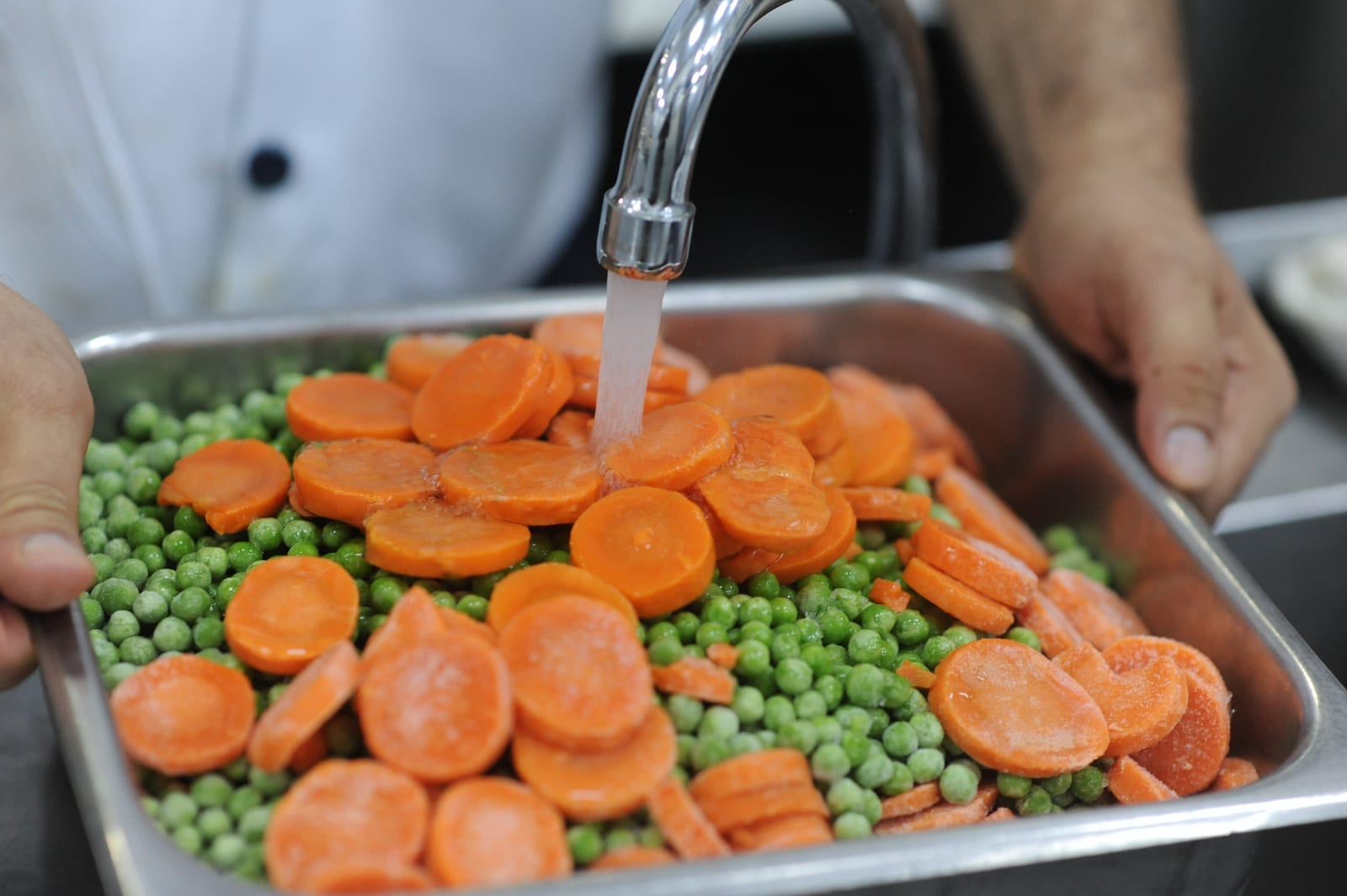 Frozen peas and carrots being rinsed before cooking